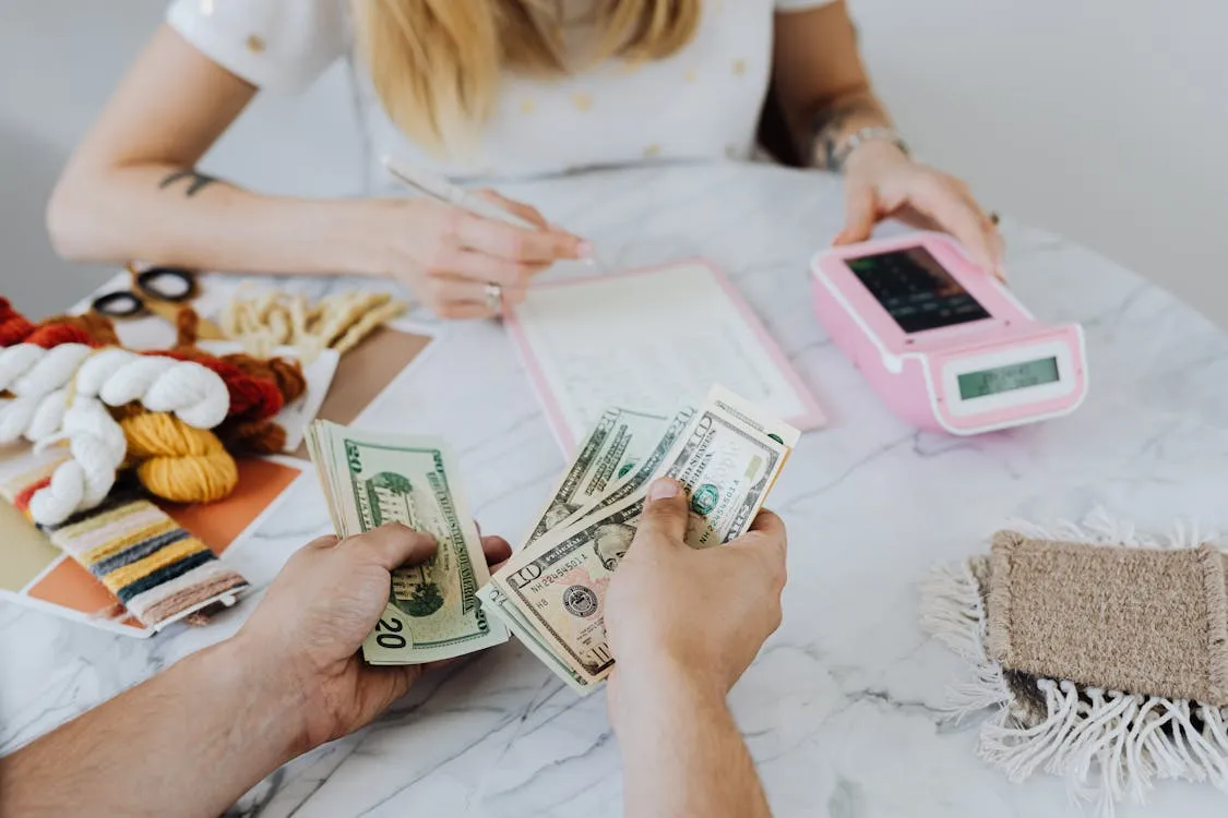 Two people counting dollar bills at a table