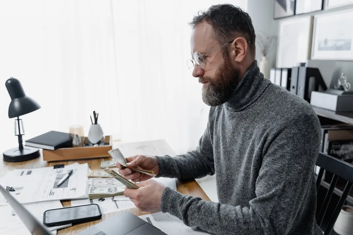 A bearded man counting piles of dollar bills