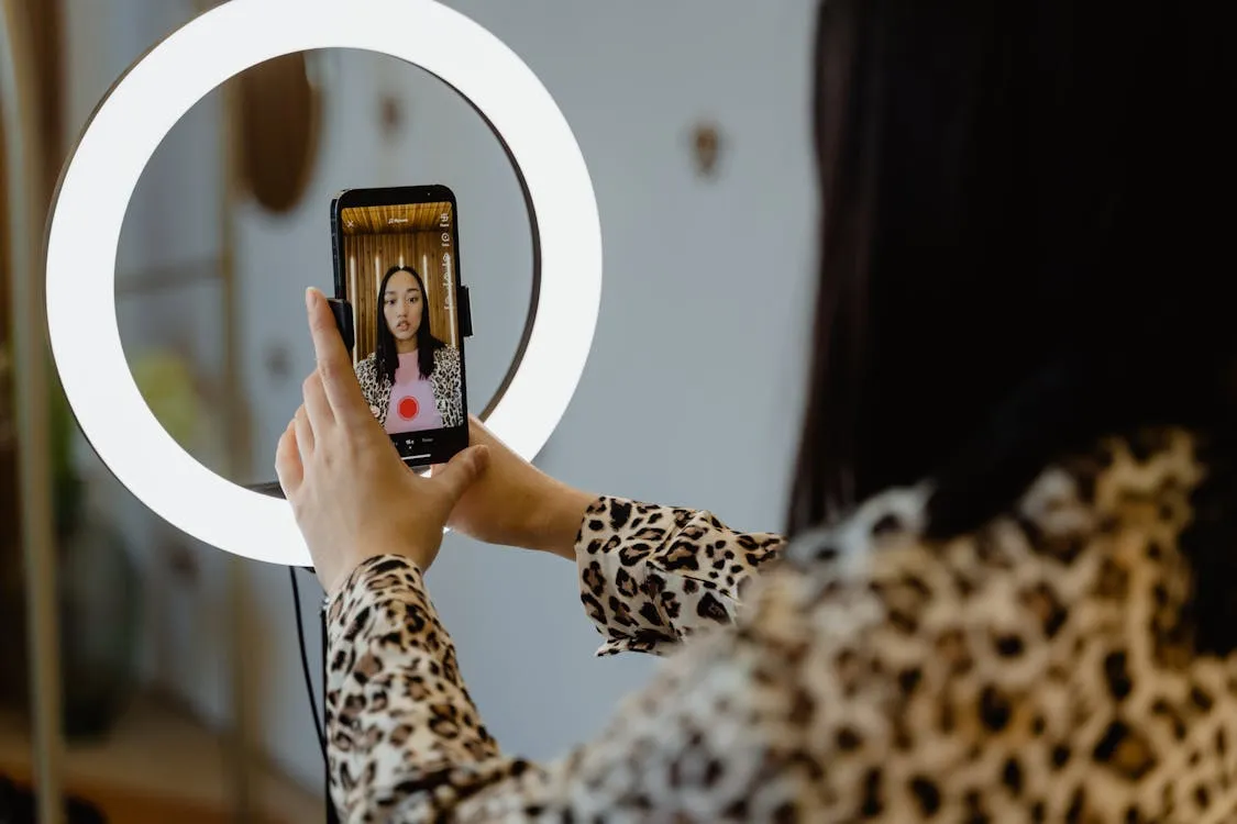A woman filming herself with a smartphone and ring light